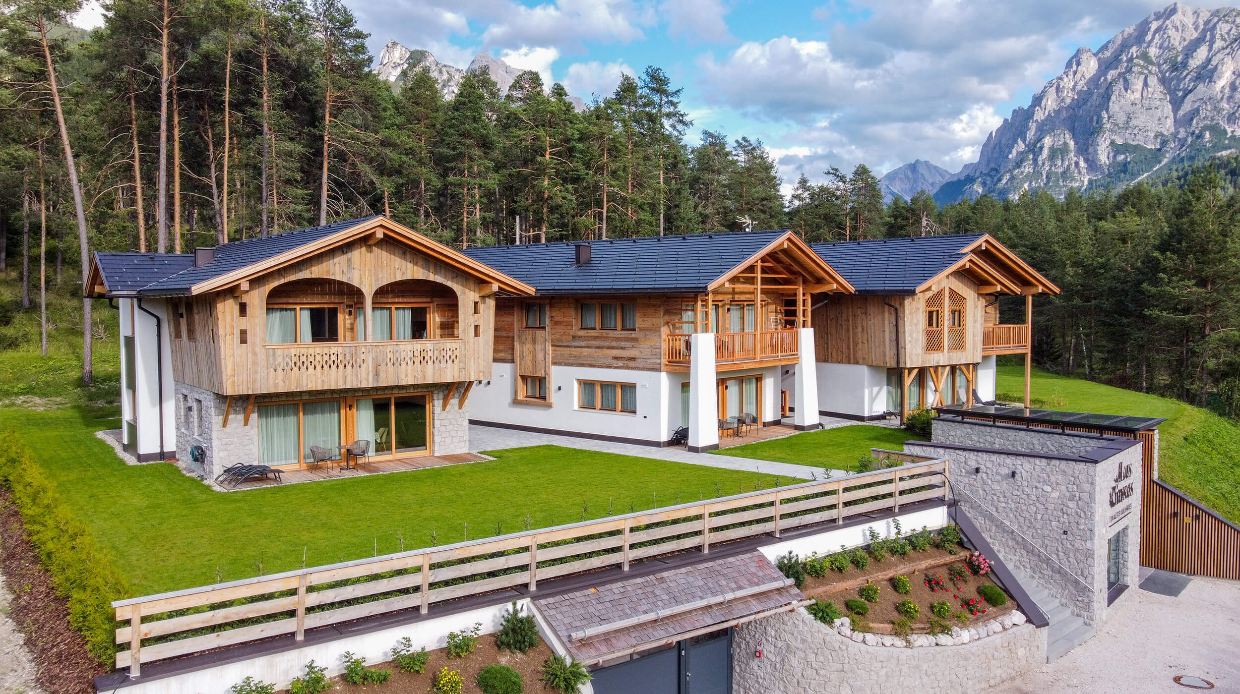 Chalets aus Natursein und Holz mit grünem Rasen - Les Ciases
